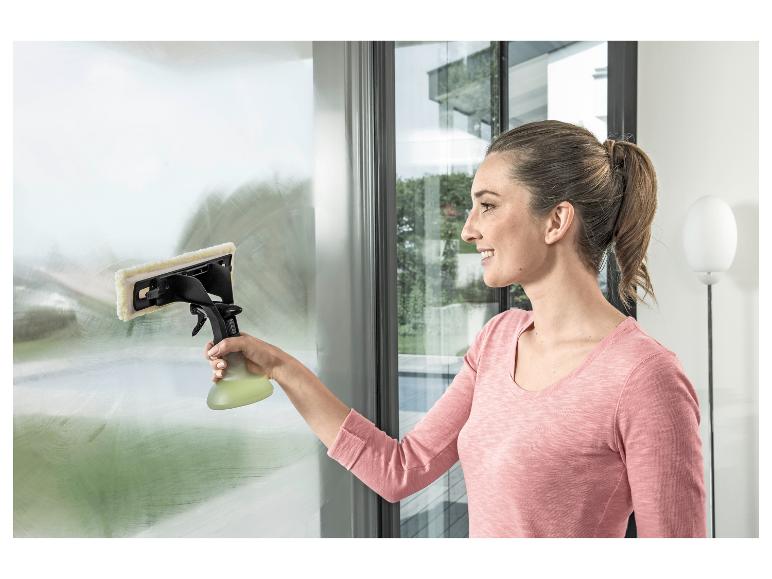 Vrouw maakt raam schoon met een raamwisser en spuitfles.