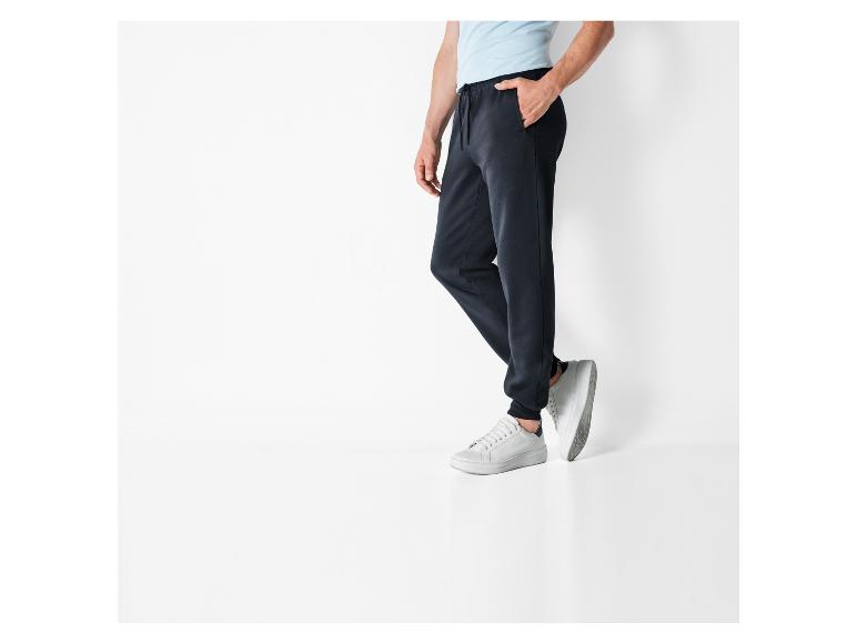 Een man draagt donkerblauwe joggingbroeken en witte sneakers.