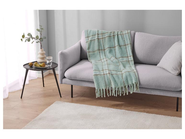 Een lichtgrijze bank met een groen en bruin geruit kleed.