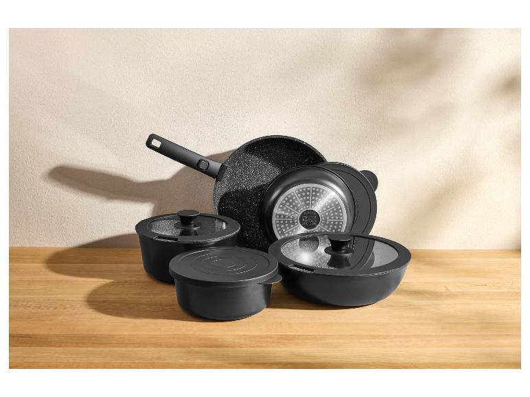 Set zwart kookgerei, inclusief een koekenpan, potten en deksels, op een houten aanrecht.