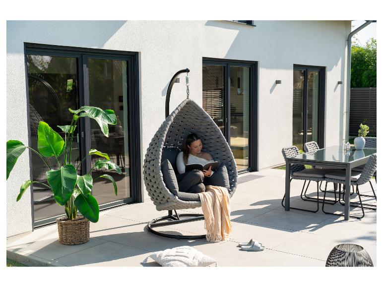 Vrouw leest in een hangstoel op een terras met eettafel en planten.