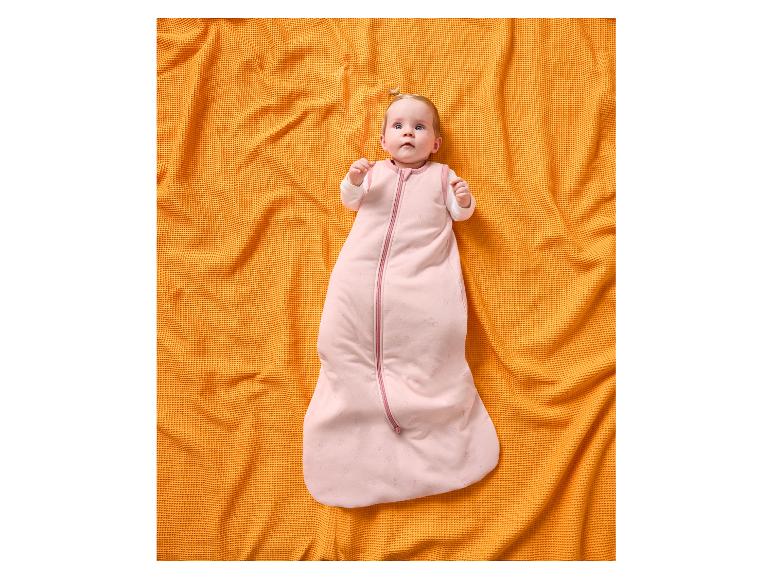 Baby in een roze slaapzak met sterren, liggend op een oranje wafeldekentje.