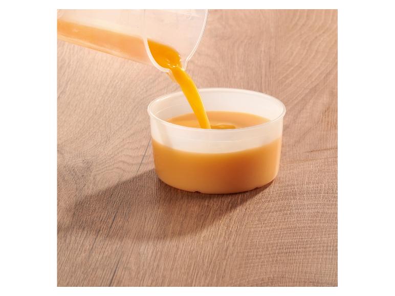 Sinaasappelsap wordt uit een kan in een beker gegoten op een houten tafel.
