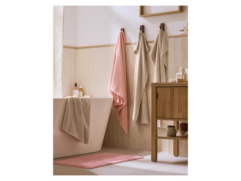 Roze en beige handdoeken in een badkamer met badkuip en kastje.
