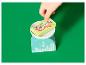 Een kinderhand plaatst 'Candy Beans' speelkaarten op een keukenweegschaal.