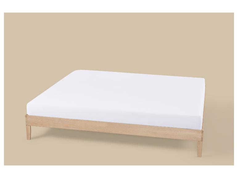 Een wit matras op een licht houten bedframe, tegen een beige achtergrond.