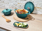 Twee turquoise gietijzeren potten met deksel, een met gebakken vlees en groenten.
