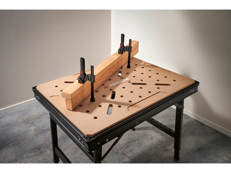 Werkbank met geperforeerd blad en twee klemmen die een houten balk vasthouden.