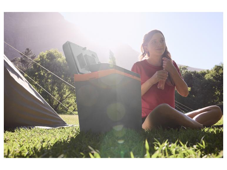 Vrouw kampeert met een draagbare koelbox, genietend van een drankje in de zon.