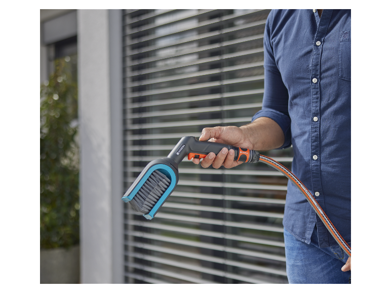 Een man houdt een Gardena hogedrukreiniger met borstel en slang vast.