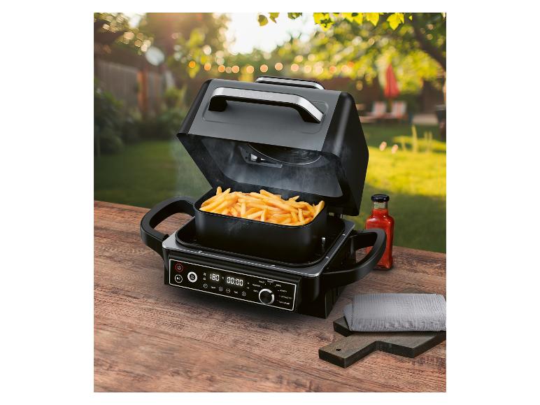 Heteluchtfriteuse met frietjes op een houten tafel in een tuin, met een ingestelde temperatuur van 180°C.