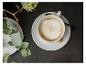 Bovenaanzicht van een cappuccino met latte art, een klein koekje en groene bladeren.