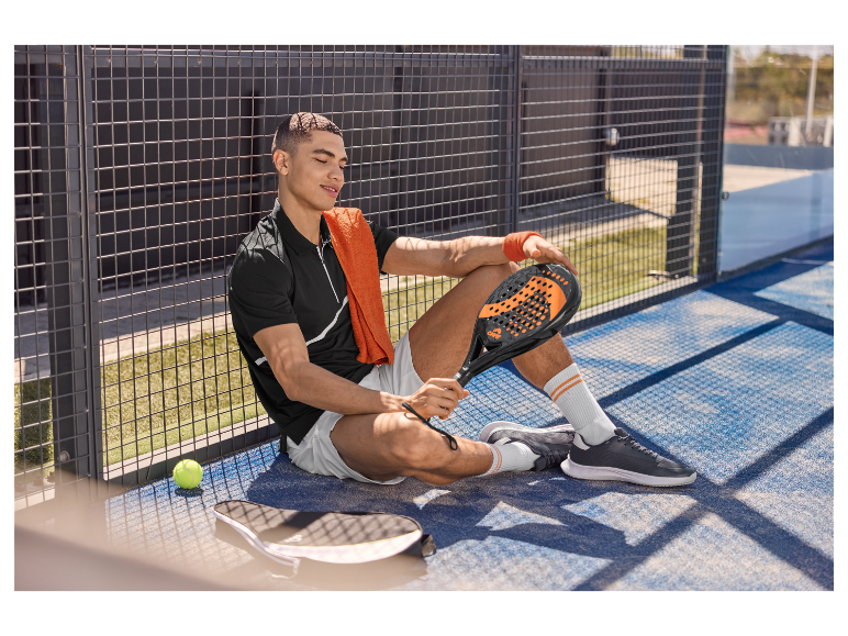 Ontspannen padeltennisser met zijn racket, zittend naast een baan.