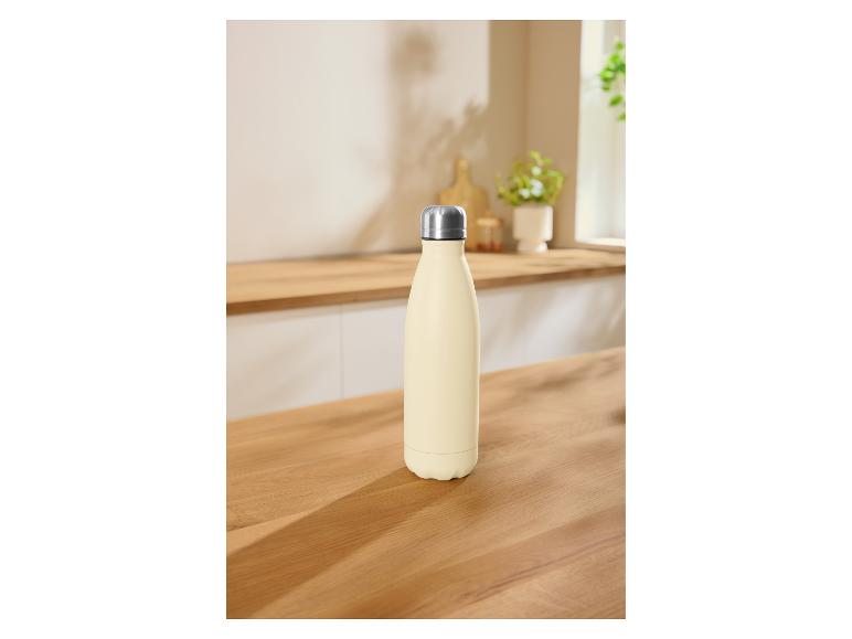 Crèmekleurige waterfles op een houten aanrecht in een lichte keuken.