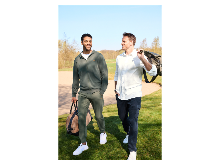 Twee mannen lopen over een golfbaan met reistassen.