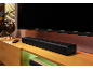 Zwarte soundbar onder een televisie, met afstandsbediening en globe op een houten meubel.