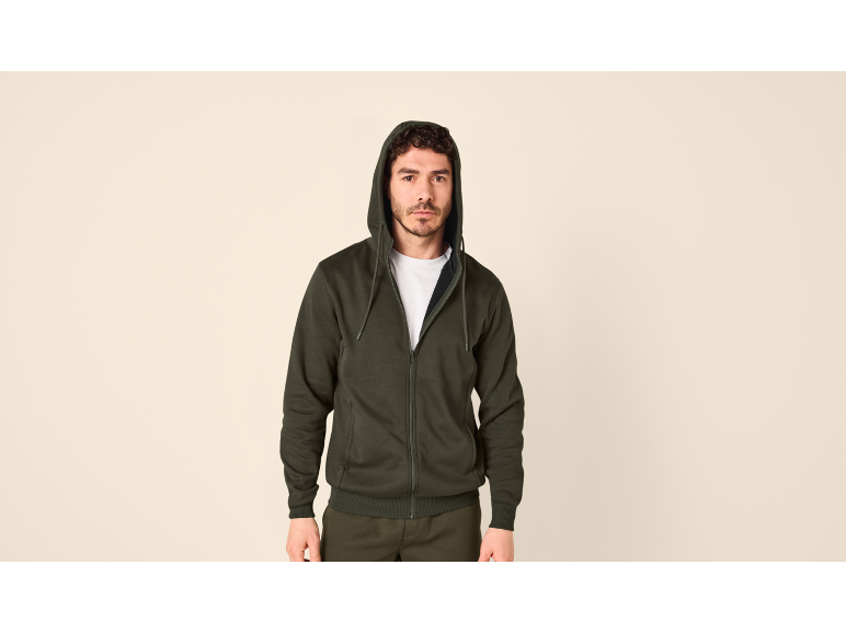 Man in donkergroene hoodie met rits, op een neutrale achtergrond.