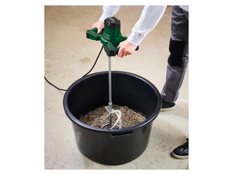 Mortelmixer in de handen van een persoon, die mortel mengt in een zwarte emmer.