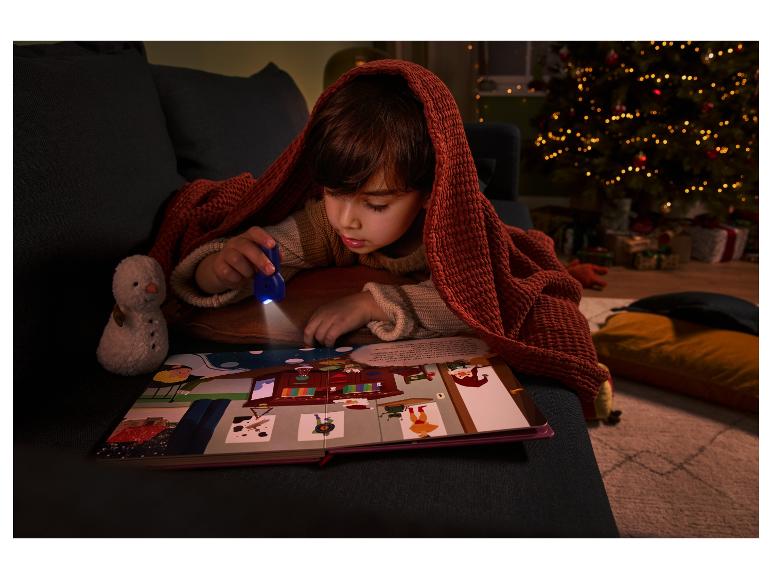 Kind leest een prentenboek met een UV-zaklamp onder een deken bij de kerstboom.