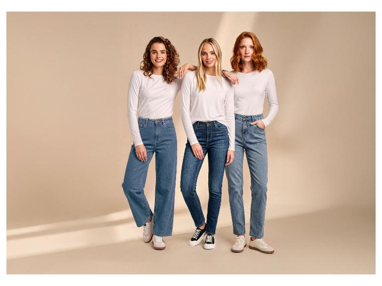 Drie vrouwen dragen witte shirts met lange mouwen en jeans, poserend tegen een beige achtergrond.