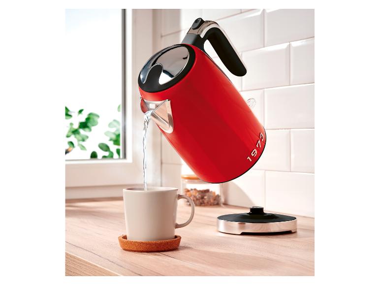Rode waterkoker met opschrift „1973” schenkt water in een mok op een houten aanrecht.