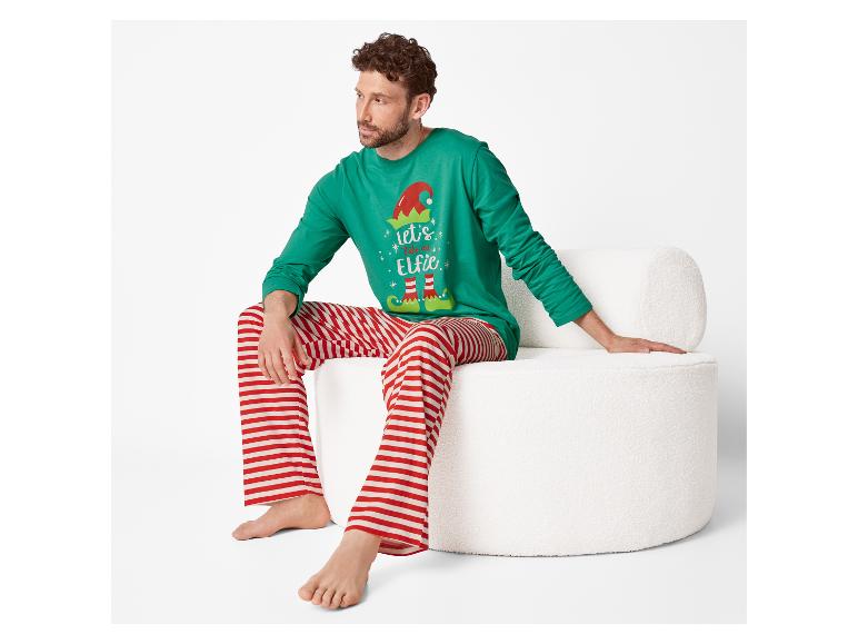 Man zit op witte stoel in groene kerstpyjama met 'let's take an Elfie' tekst en rood-wit gestreepte broek.