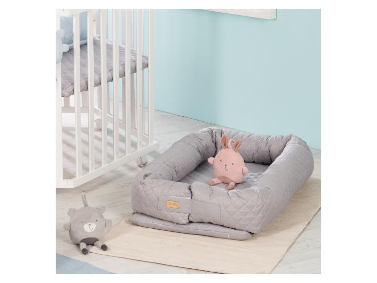 Babynest met roze konijn en grijze beer knuffels naast een wit ledikant