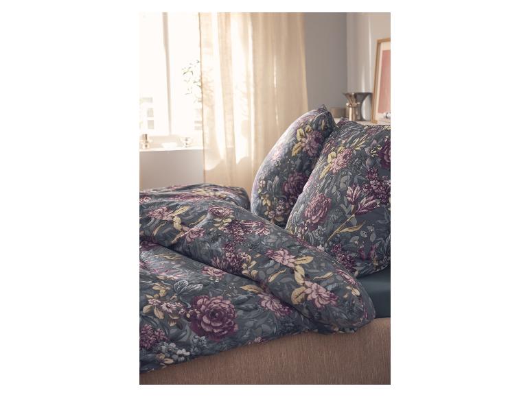 Dekbedovertrek en kussens met bloemenprint in een slaapkamer met lichte gordijnen.