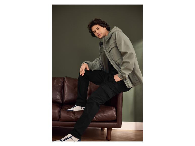 Man in grijsgroene jas, zwarte broek en wit-blauwe sneakers.