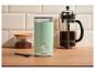 Mintgroene koffiemolen, French press koffiezetapparaat en pot gemalen koffie op een houten tafel.