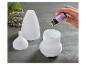 Een hand druppelt lavendelolie in een witte aroma diffuser, met gedroogde lavendel op de achtergrond.