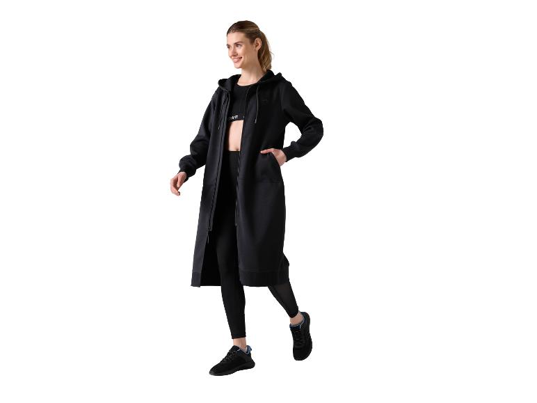 Vrouw in een zwarte lange jas met capuchon, legging en Crivit sportbeha.