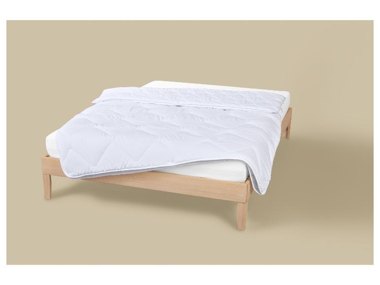 Wit gewatteerd dekbed op een houten bedframe met een wit matras.