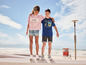 Twee kinderen dragen T-shirts met Malibu en Californië-thema's op het strand.