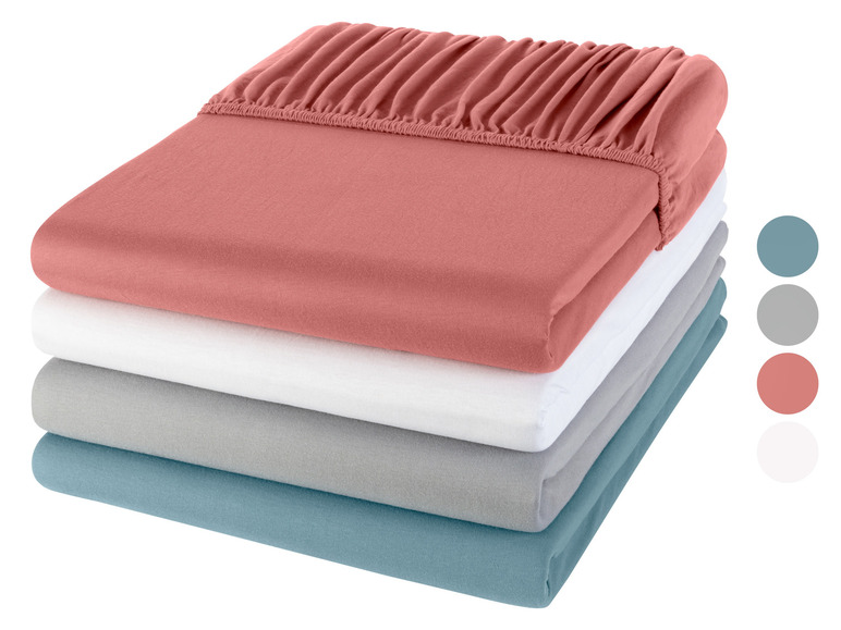 Een stapel bedlakens in verschillende kleuren: roze, wit, grijs en blauw.