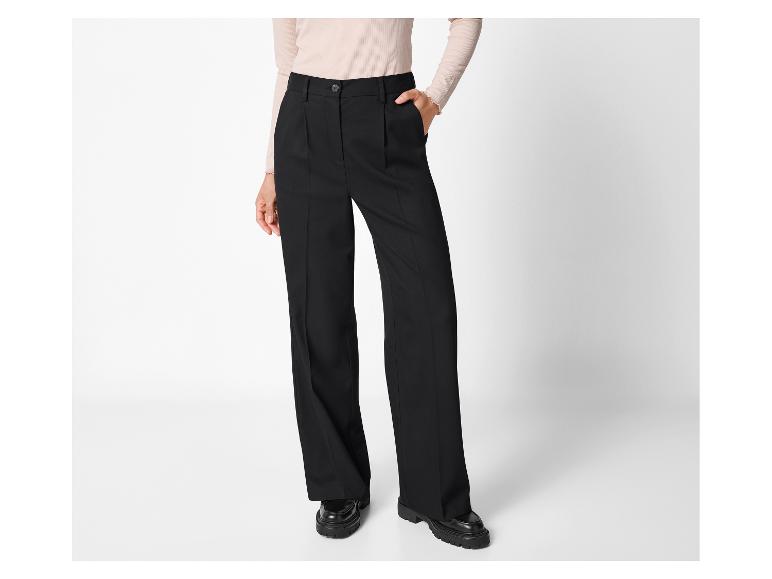 Zwarte damesbroek met plooien en beige blouse, gecombineerd met zwarte loafers