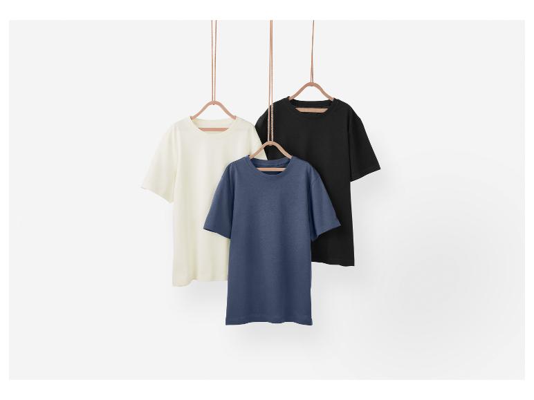 Drie effen t-shirts hangen aan houten hangers.