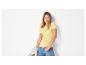Vrouw in geel geribbeld T-shirt en blauwe jeans, met beige jas.