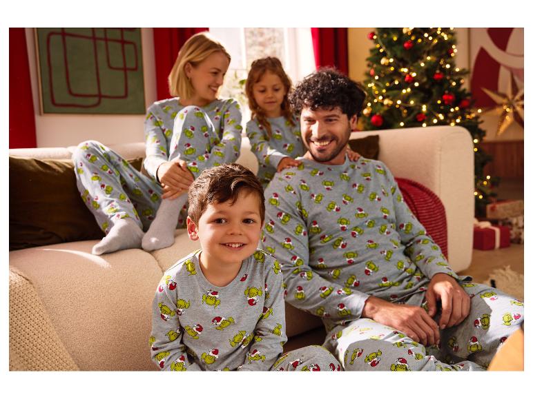 Familie in bijpassende Grinch-pyjama's, zittend op een bank bij een kerstboom.