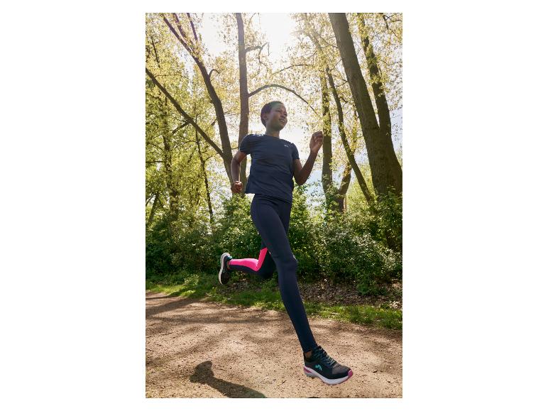 Vrouw rent door het bos in sportkleding en Kalenji schoenen.