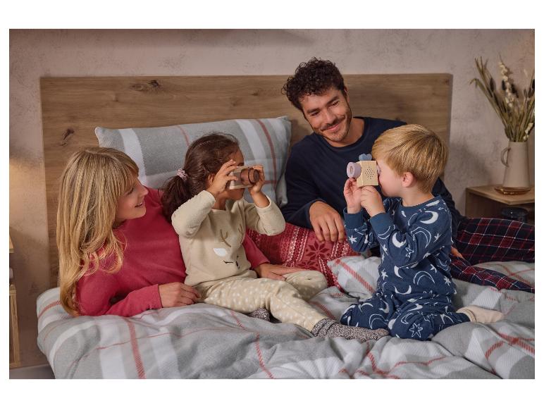 Een familie in pyjama op een bed, met kinderen die spelen met speelgoedcamera's.