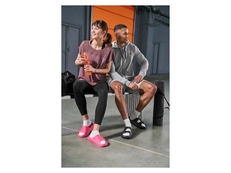 Vrouw en man in sportkleding en slippers zitten op een bank na het sporten.