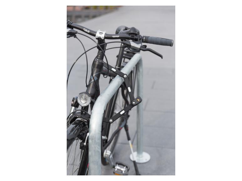 Een zwarte fiets met een vouwslot vastgemaakt aan een metalen fietsenrek.