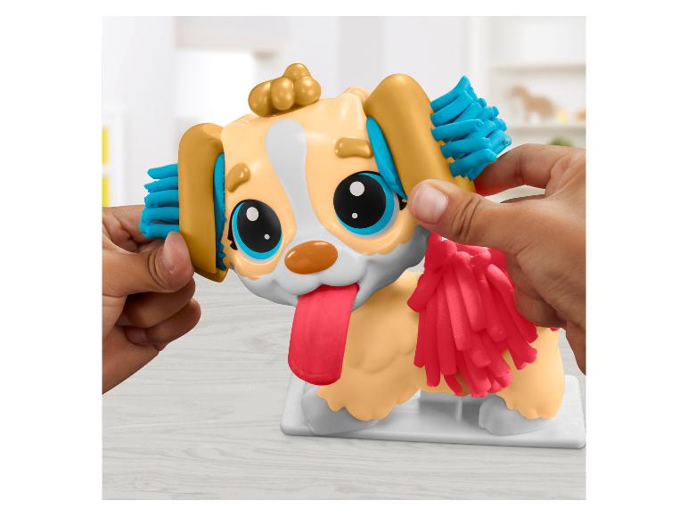 Handen vormen klei op een speelgoedhond met grote ogen en uitgestoken tong.