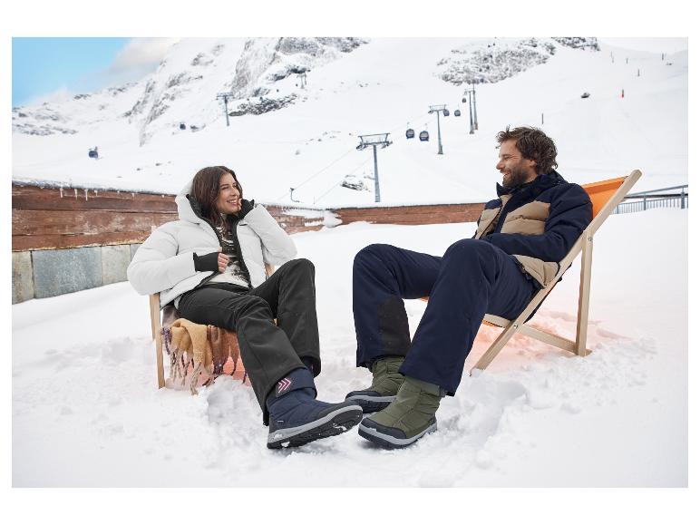 Twee mensen ontspannen in strandstoelen op sneeuw, gekleed in ski-jassen en -broeken.