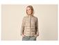 Vrouw in een beige gewatteerde jas en groene broek, met handen in de zakken.