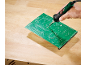 Een hand soldeert een groene printplaat op een houten werkbank.