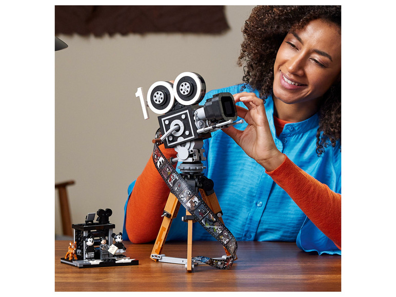 Een persoon die een LEGO Mickey Mouse filmcamera bouwt met een filmrol met iconische Disney-figuren.