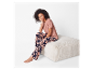 Model in een bloemen pyjama en roze t-shirt zit op een poef.