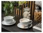 Twee koffiekopjes, één met cappuccino, naast bloemen en koekjes.